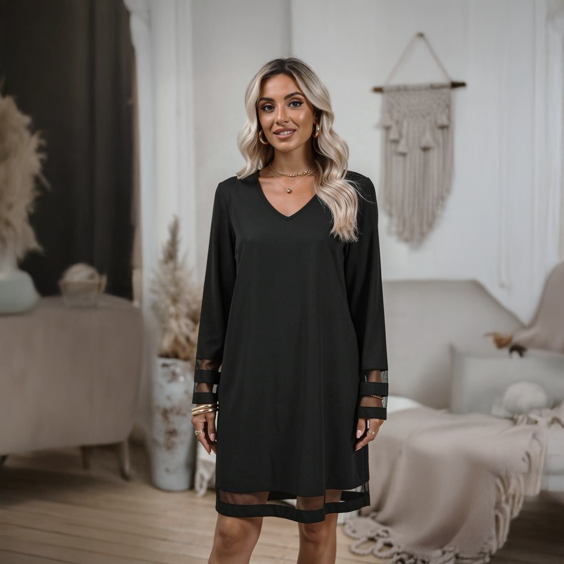 Structured black midi dress with a smooth base fabric and dramatic sheer tulle detailing on the sleeves or overlay, photographed in a modern Raouche apartment.
