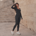 Sleek black long-sleeve performance suit for women, featuring a front zip and a sculpted, second-skin fit, photographed on an old street in Zahle.
